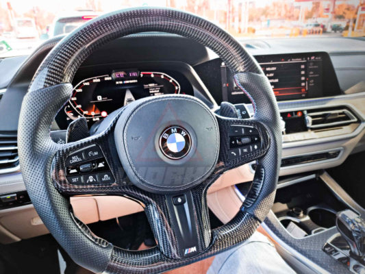 Cockpit view of a BMW G05 X5 M Sport, featuring a custom design m sport steering wheel, with gloss black carbon fiber, black perforated leather and carbon fiber paddle shifters.